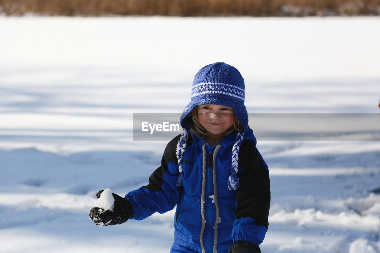 Little boy holding snowball outside in blue snowsuit