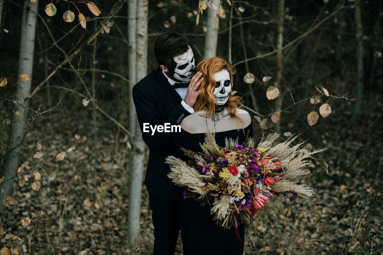 A couple in love celebrates halloween in costumes and makeup with a bouquet of dried flowers