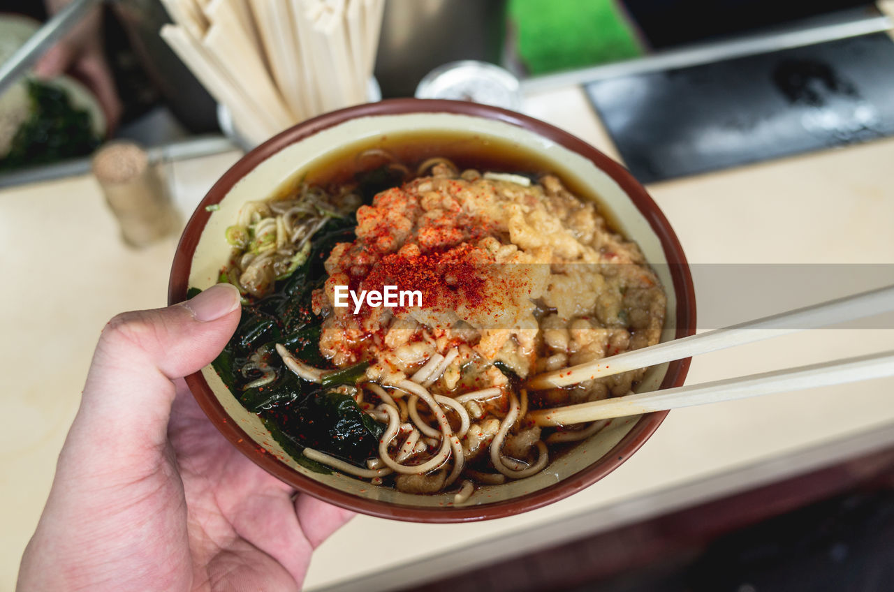 Close-up of human hand holding noodle soup in bowl