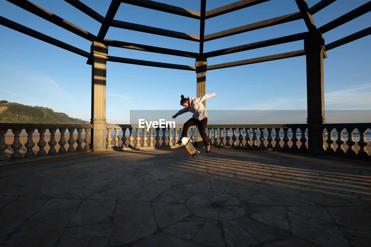 Dynamic male skater jumping with skateboard on tiled terrace at sunset in summer and performing stunt