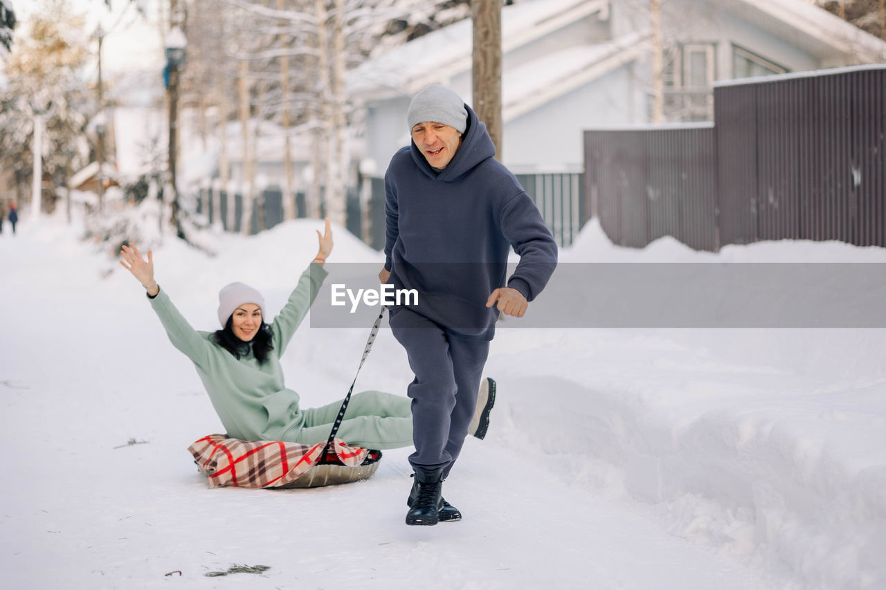 Smiling man giving sledding ride to woman. love and leisure concept.