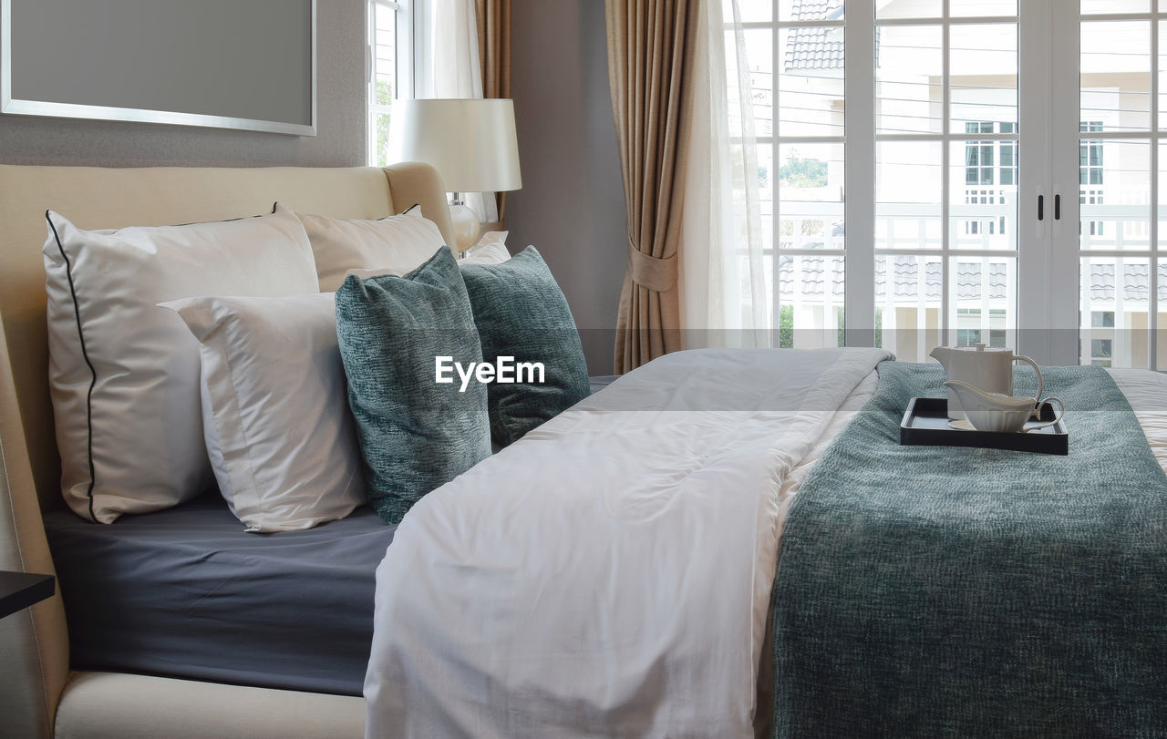 MIDSECTION OF WOMAN RELAXING ON BED AGAINST WINDOW AT HOME