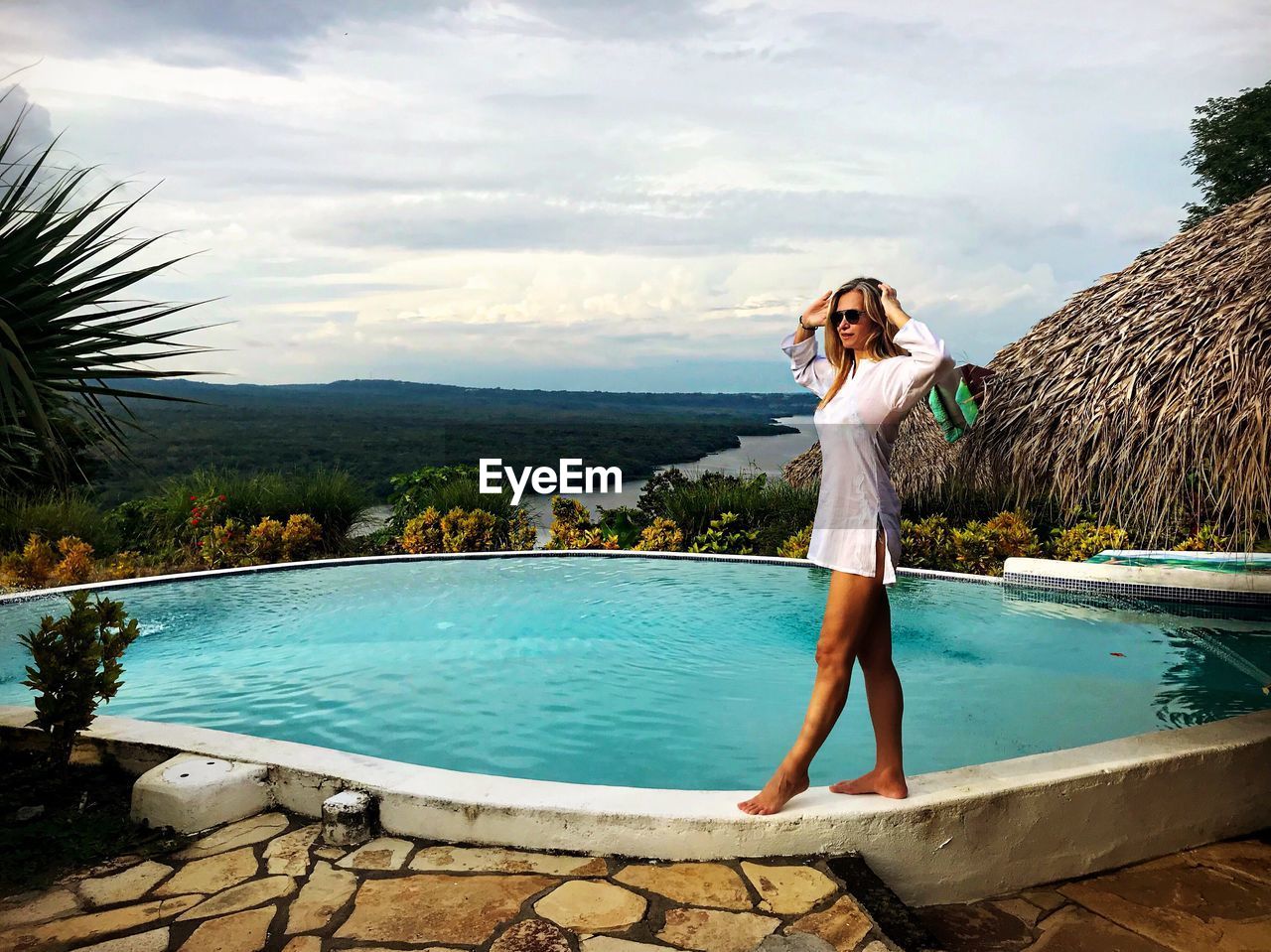 Full length of young woman standing at poolside against sky