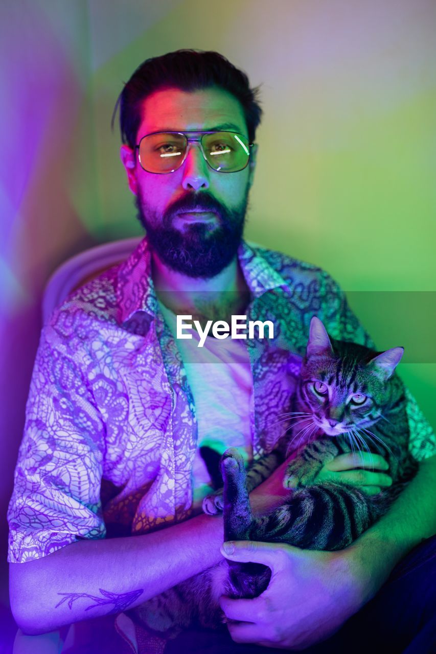 PORTRAIT OF YOUNG MAN WITH CAT AGAINST WALL