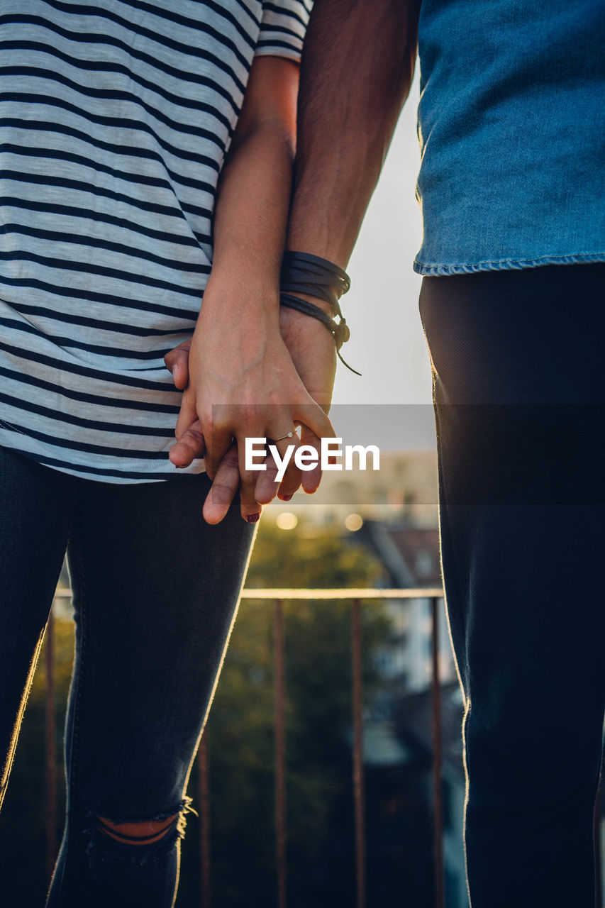 Midsection of couple holding hands against sky