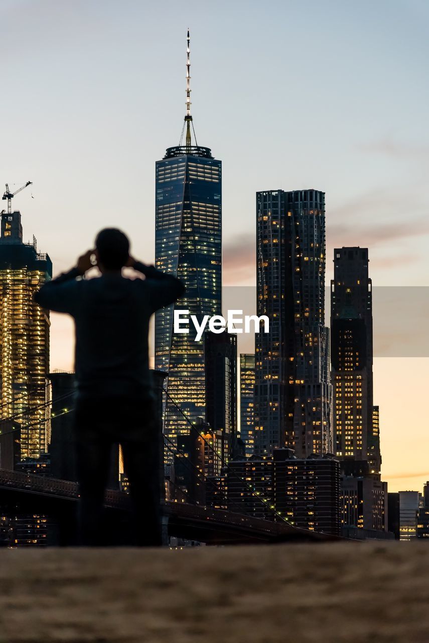 Rear view of man against brooklyn bridge and one world trade center in city