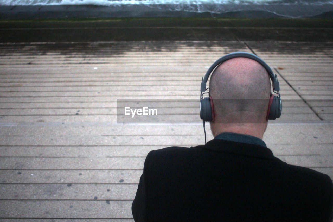 Rear view of man listening music through headphones