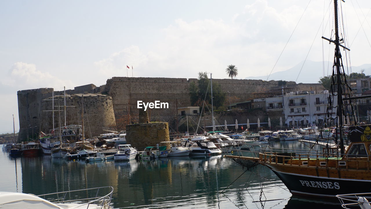 SAILBOATS MOORED ON CANAL AGAINST BUILDINGS IN CITY