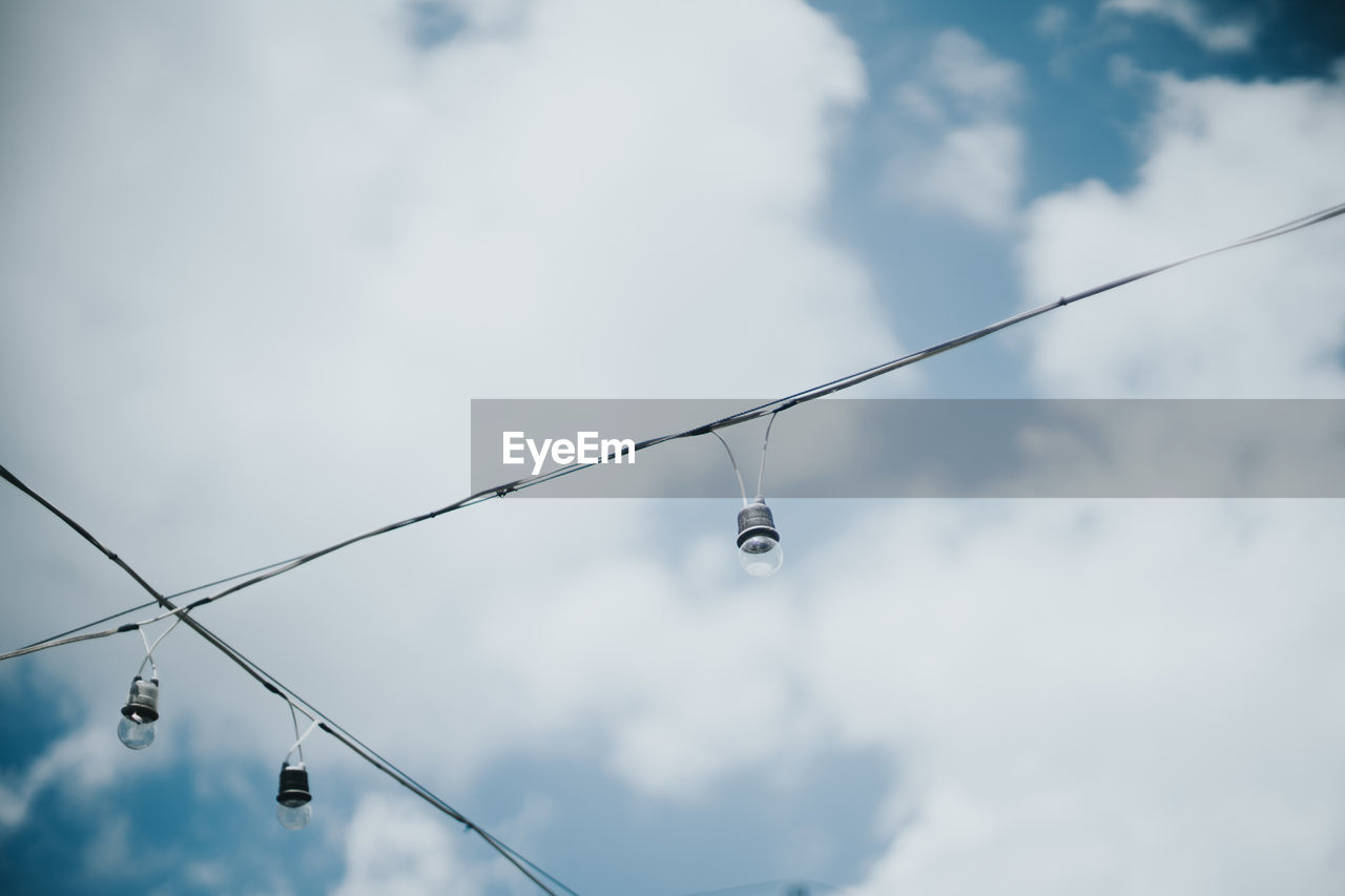 Low angle view of light bulbs against cloudy sky