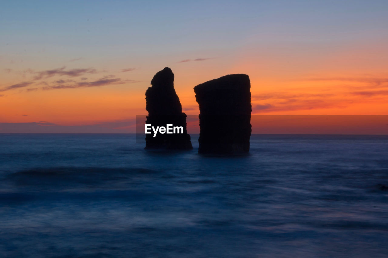 Silhouette rock on sea against romantic sky at sunset