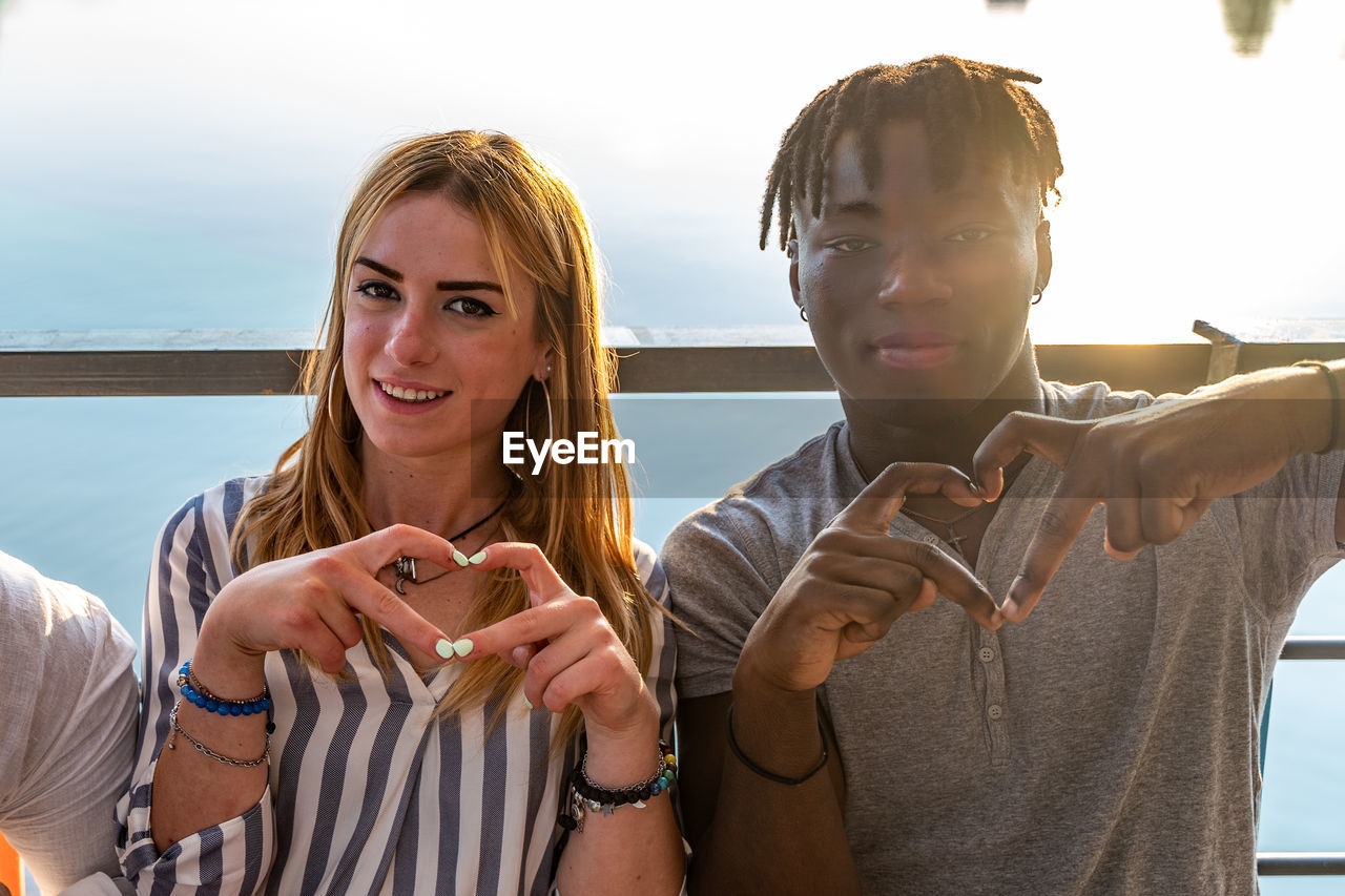 Small group of young adult multiethnic friends showing heart sign with hands - vacation concept 