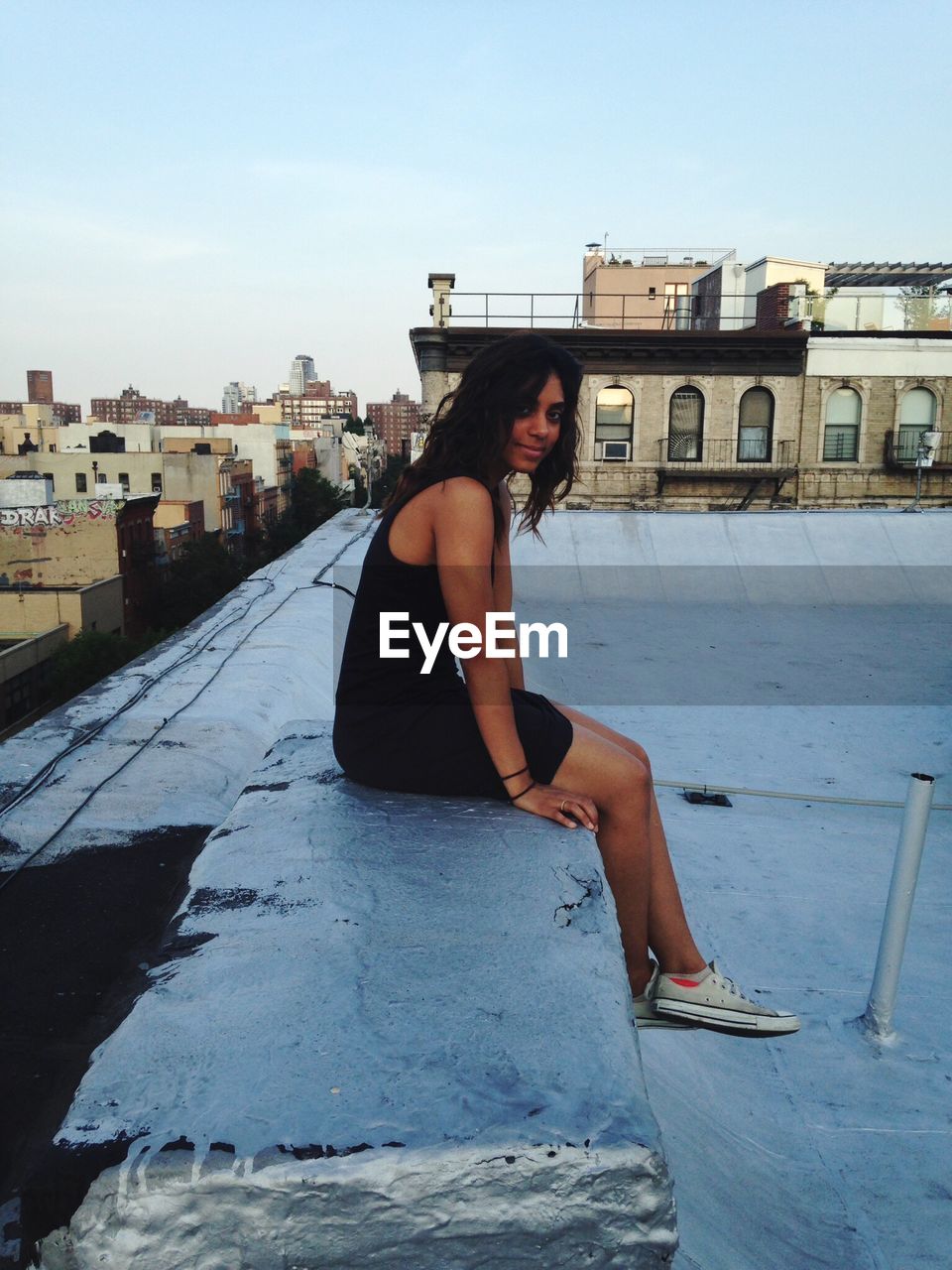 Side view portrait of young woman sitting on retaining wall at terrace