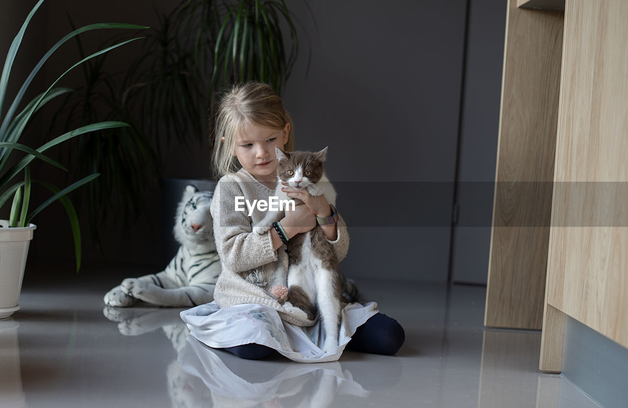 A little girl sits on the floor and holds a cat in her hands