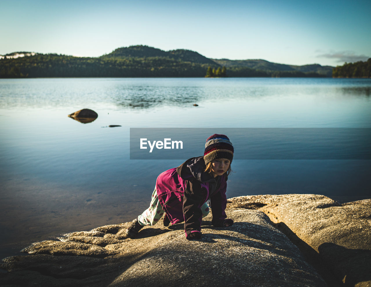 Girl standing on rock by lake against sky