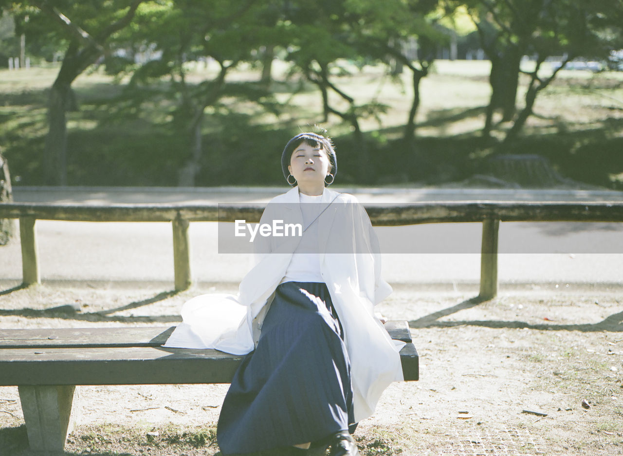 Woman sitting on bench with eyes closed at park
