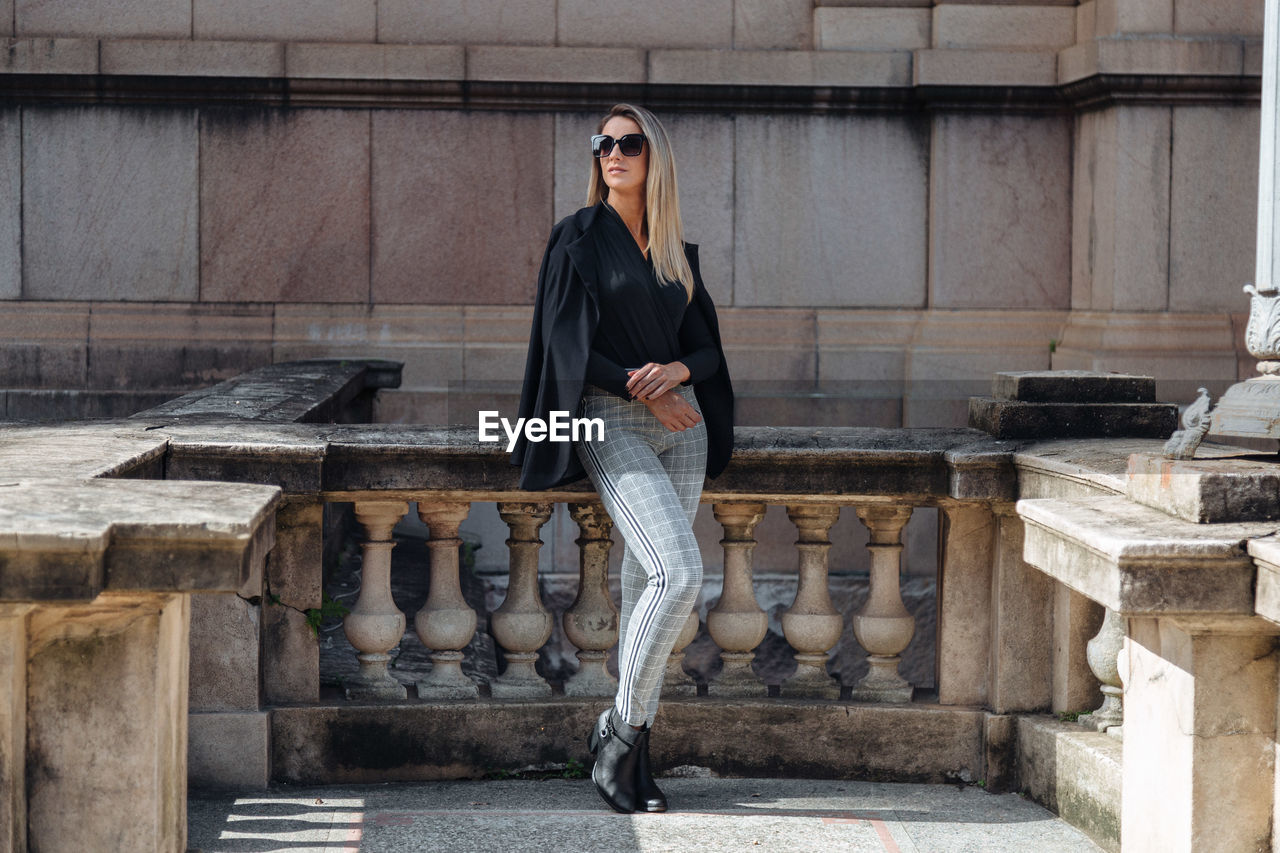 Woman wearing sunglasses looking away while standing against building