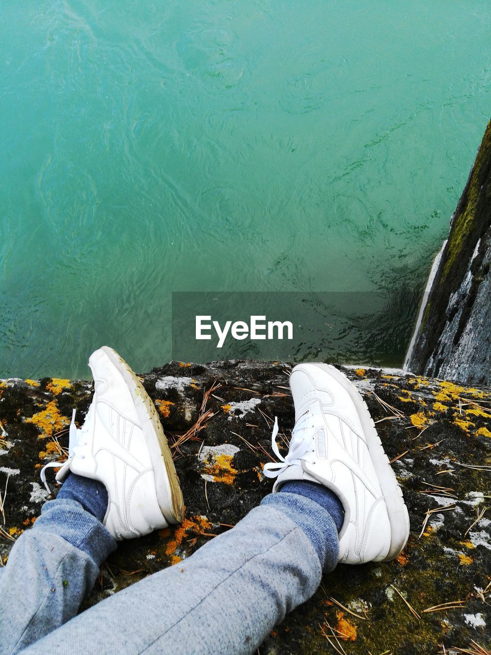 Low section of person wearing shoes while lying by lake