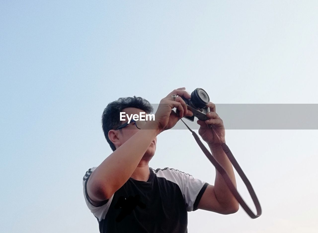 Man photographing with camera against clear sky