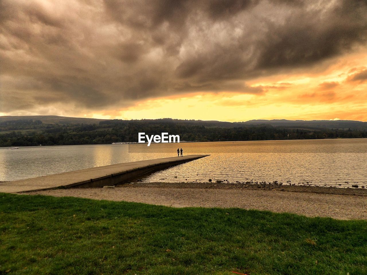 Pier at river against cloudy sky during sunset