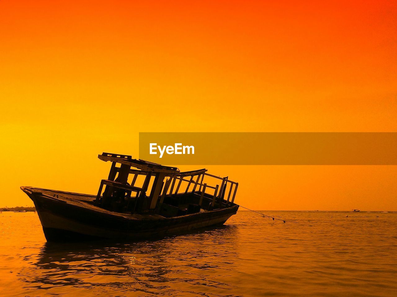 Boat moored on sea against orange sky at sunset