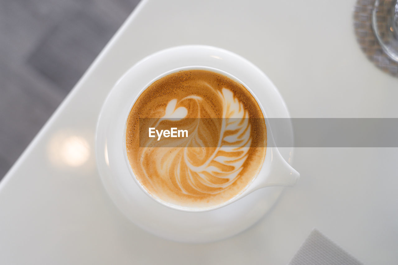 Top view of hot coffee with latte art in a white cup and saucer on white table.