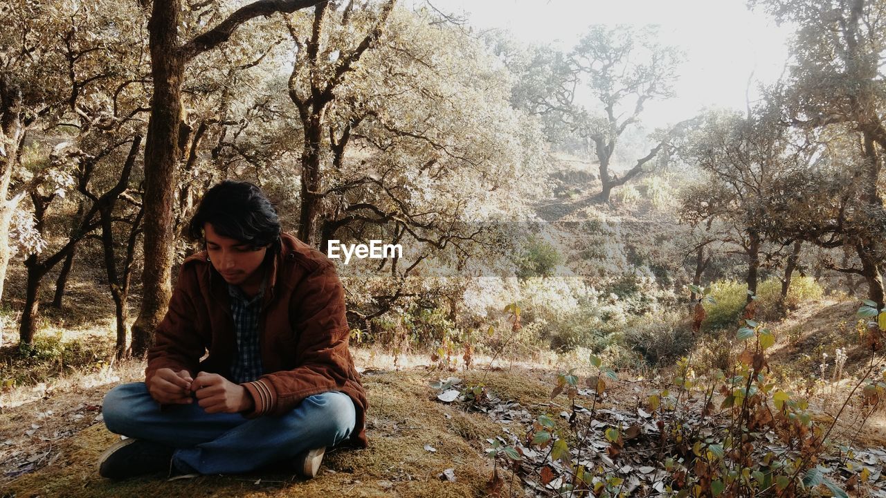 Young man sitting against trees on field at forest