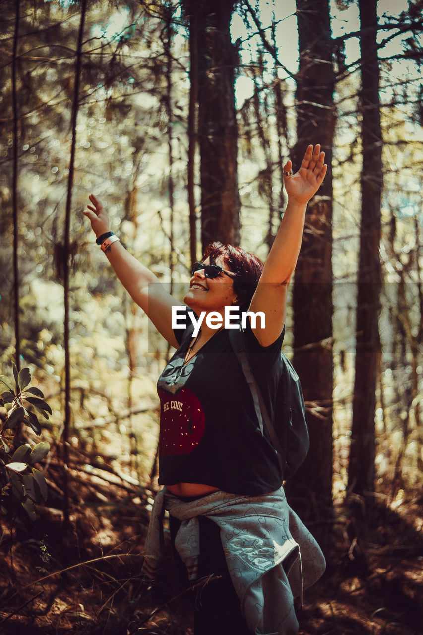 Side view of woman with arms raised standing in forest