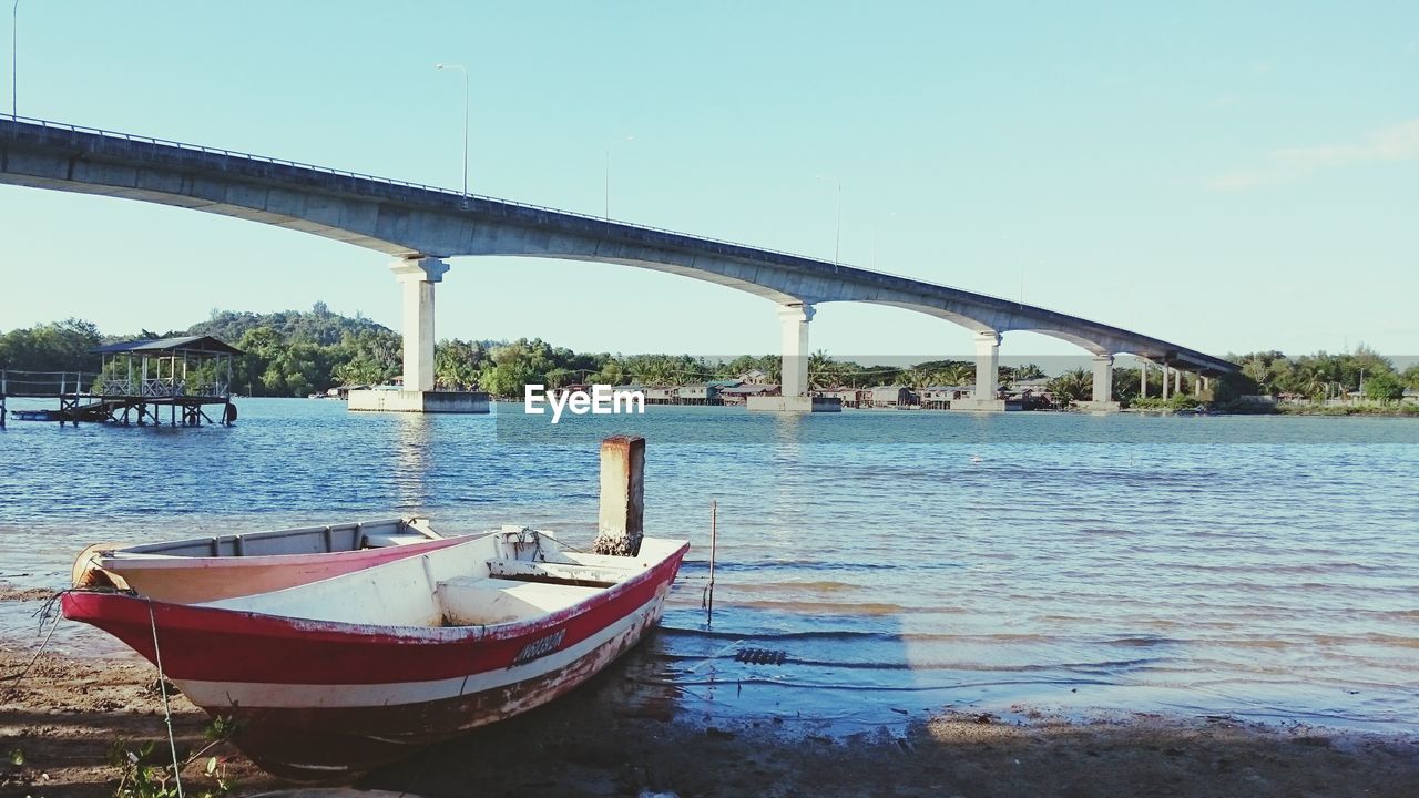 Boat moored on lakeshore with bridge in background