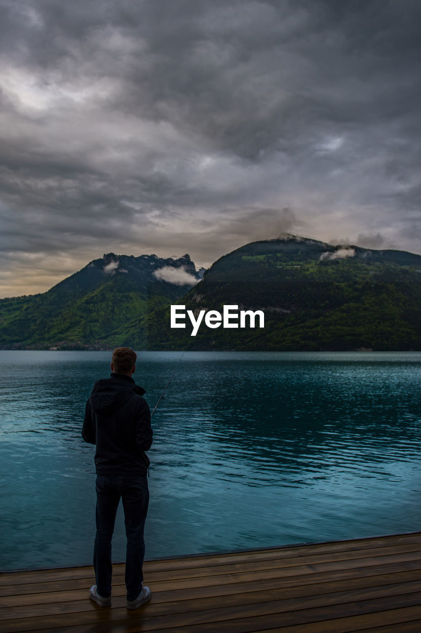 Rear view of man looking at lake against mountain range