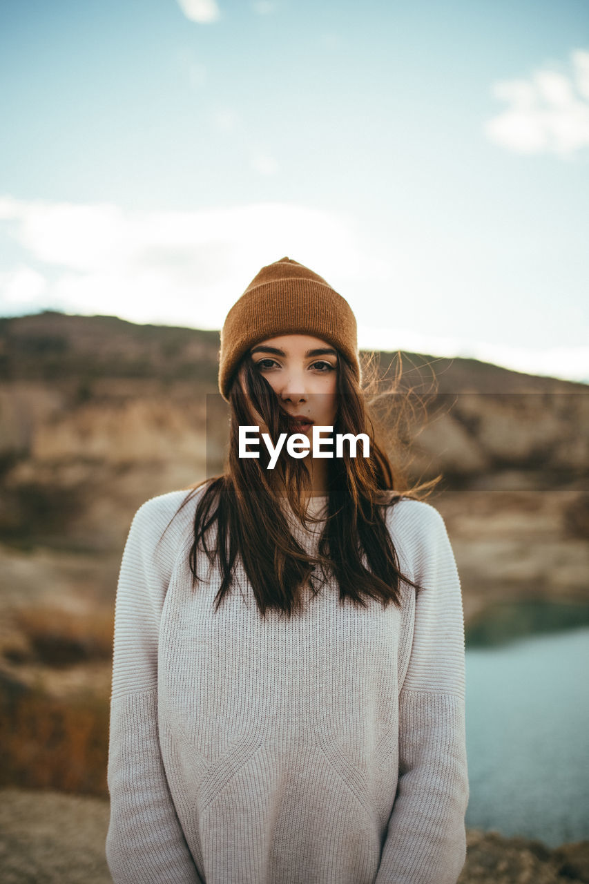 Youthful charming female tourist looking at camera while enjoying weekend journey to lake in autumn