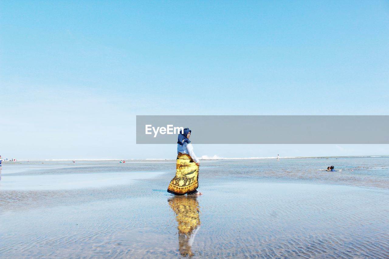 Woman walking at beach against clear blue sky