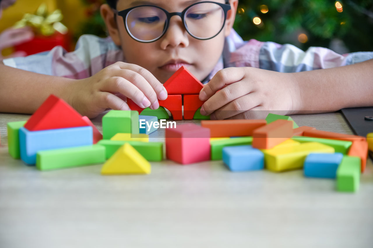 Boy playing with colorful toy blocks on table at home