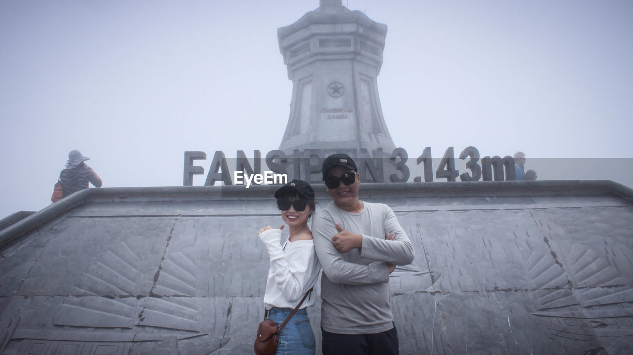 MAN AND WOMAN STANDING AGAINST STATUE