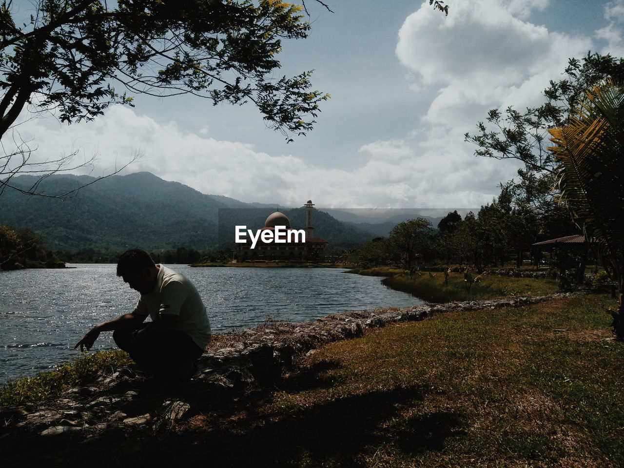 Man sitting by river against sky