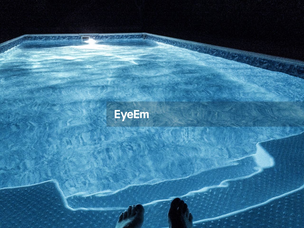 Low section of person dangling feet in swimming pool