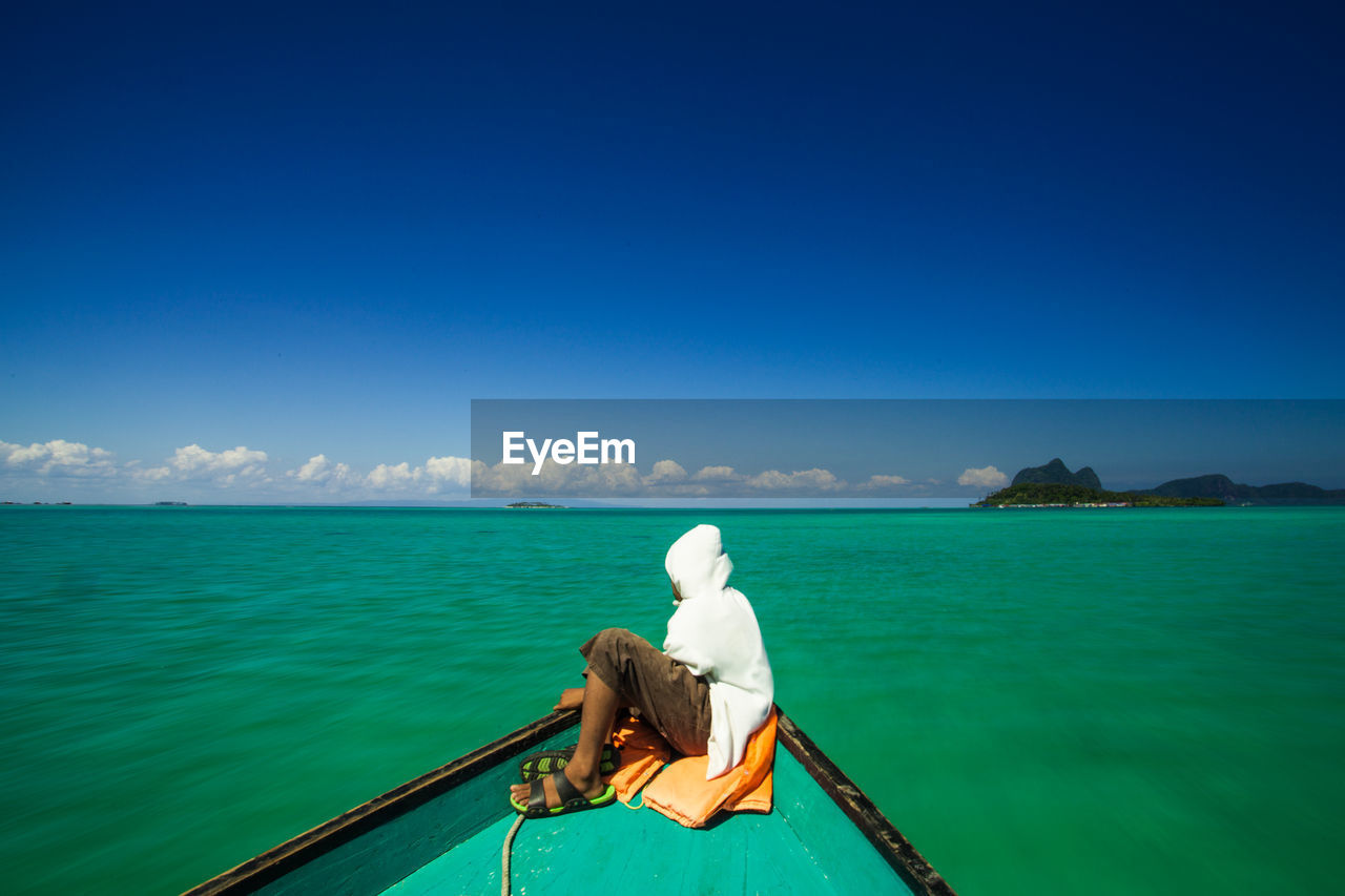 Side view of man sitting in boat on sea against blue sky