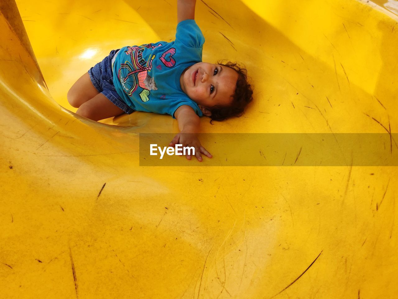 High angle view of little girl lying on slide at playground