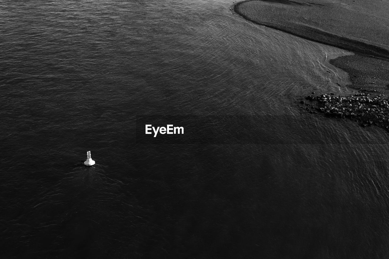 Black and white tone, aerial view single floating buoy anchor on deep dark river near coast.