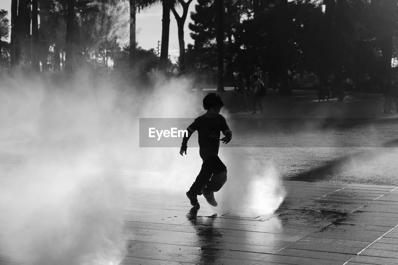 Full length of silhouette boy running amidst fountain in city