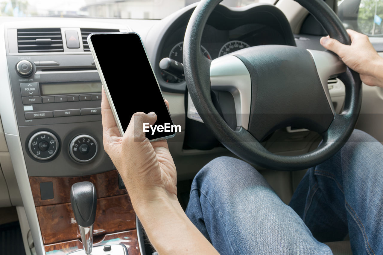 Midsection of man using mobile phone in car