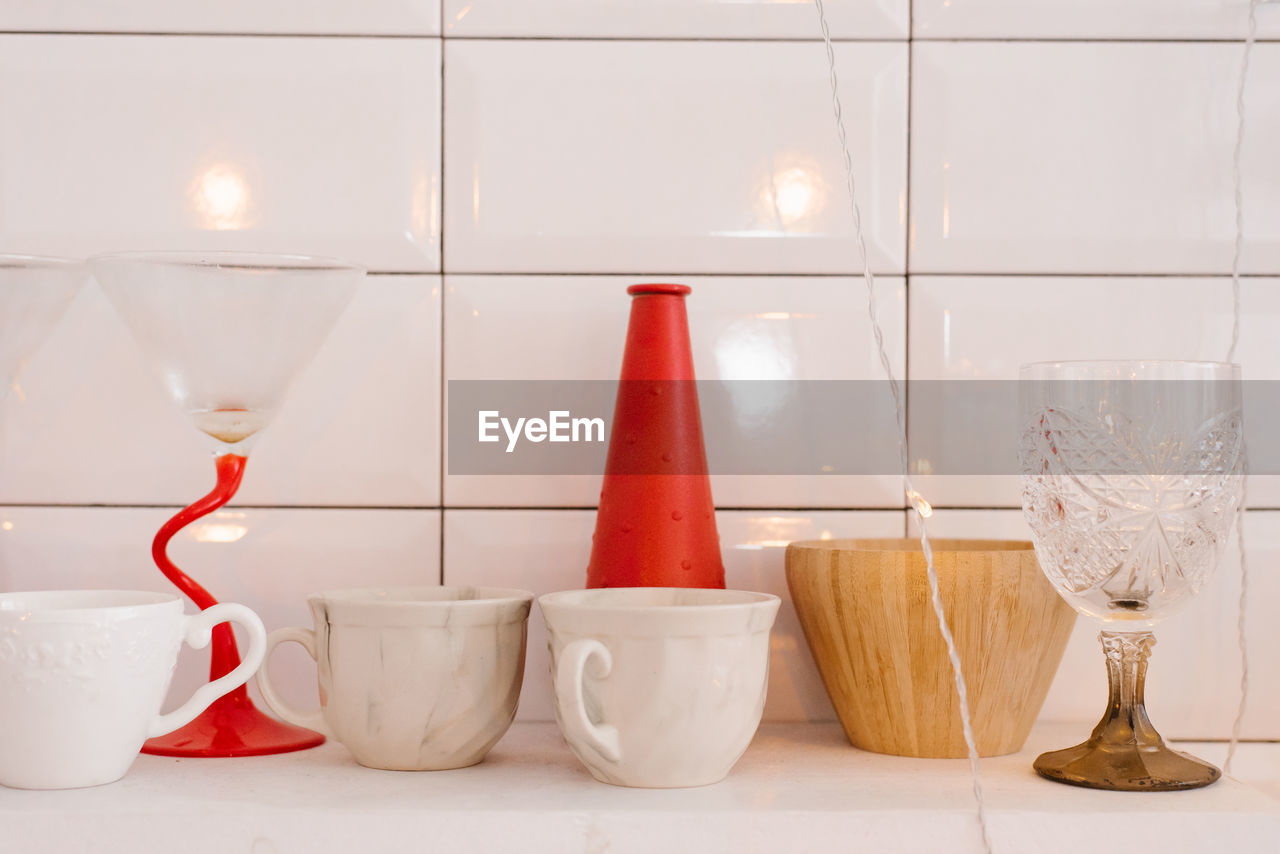 White porcelain or ceramic mugs, wooden crockery, red vase and wine glass on the kitchen shelf