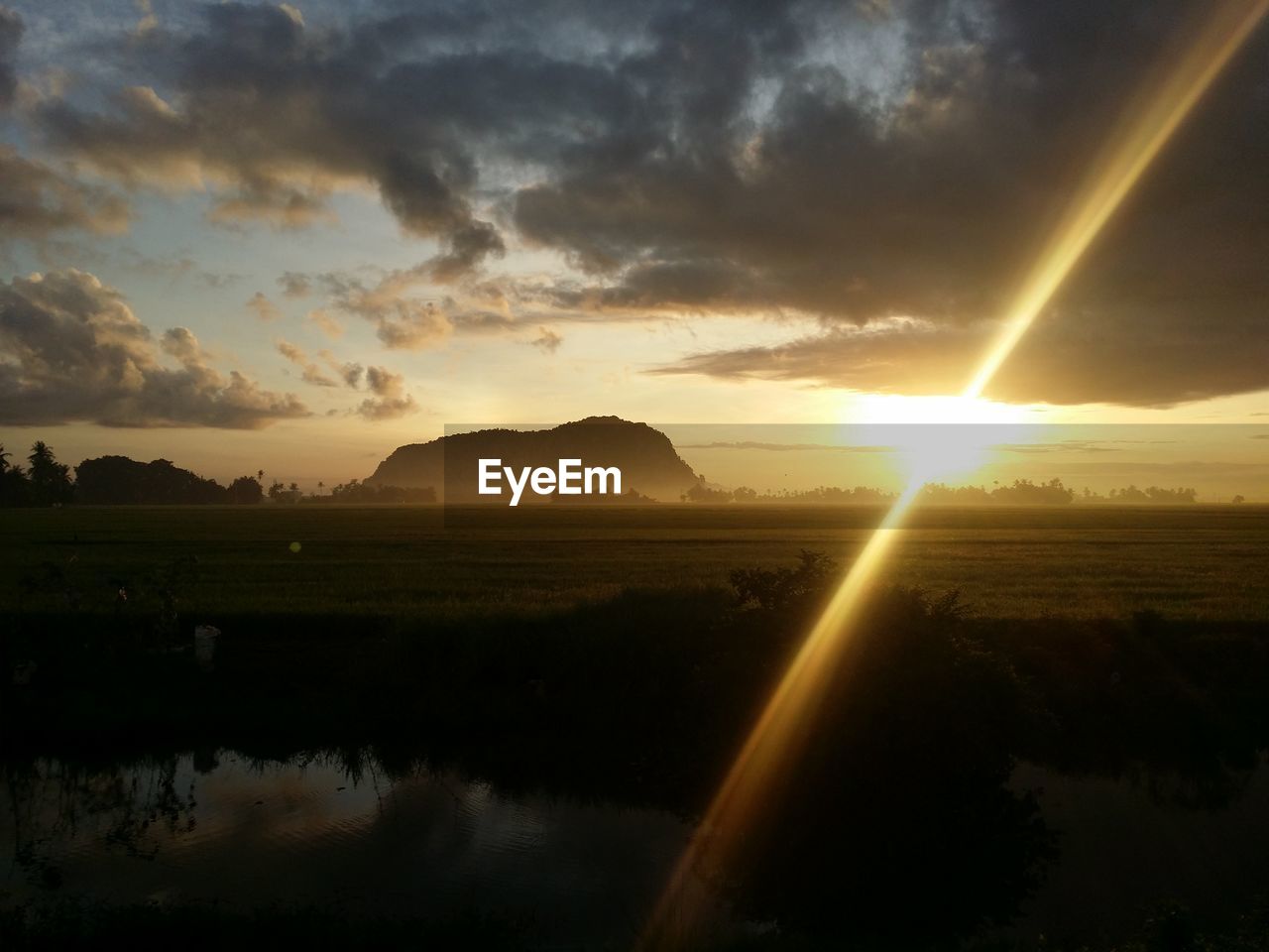 River by field against sky during sunset