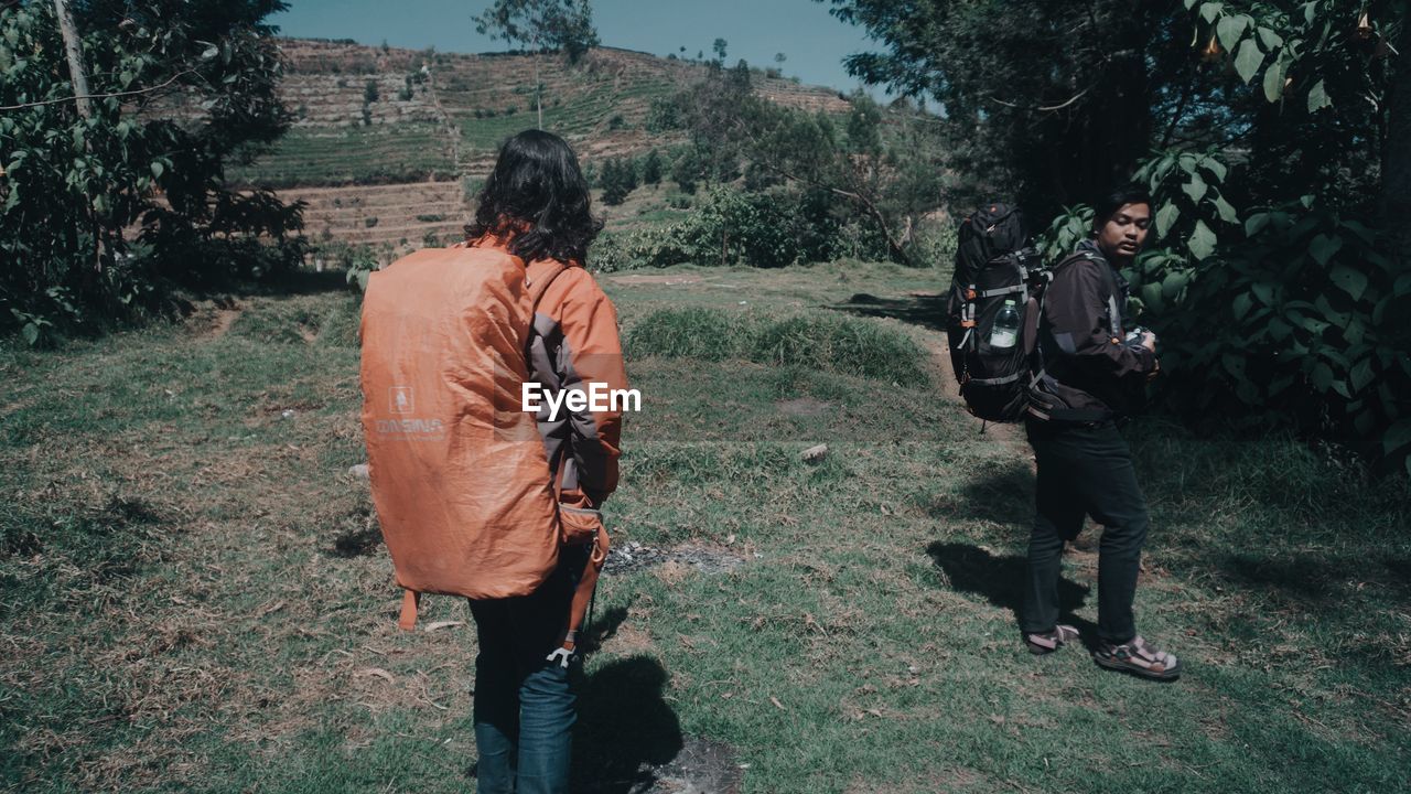 REAR VIEW OF PEOPLE WALKING ON LAND BY TREES