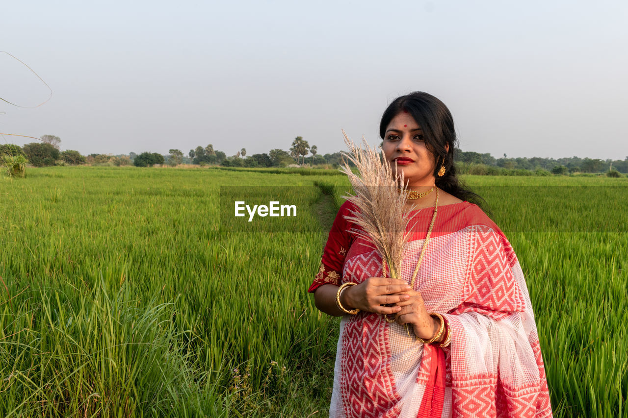 A beautiful indian woman wearing a traditional sari and jewelry stands on a paddy field background