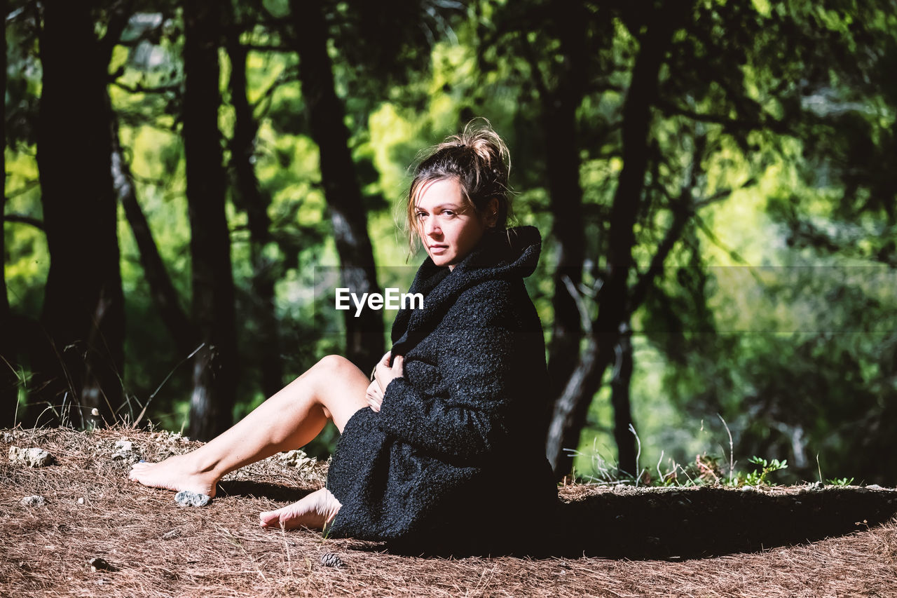 Young woman sitting on tree trunk in forest