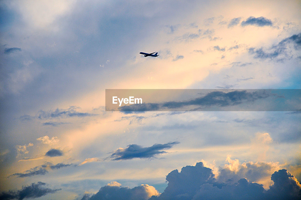 Low angle view of airplane flying in sky during sunset