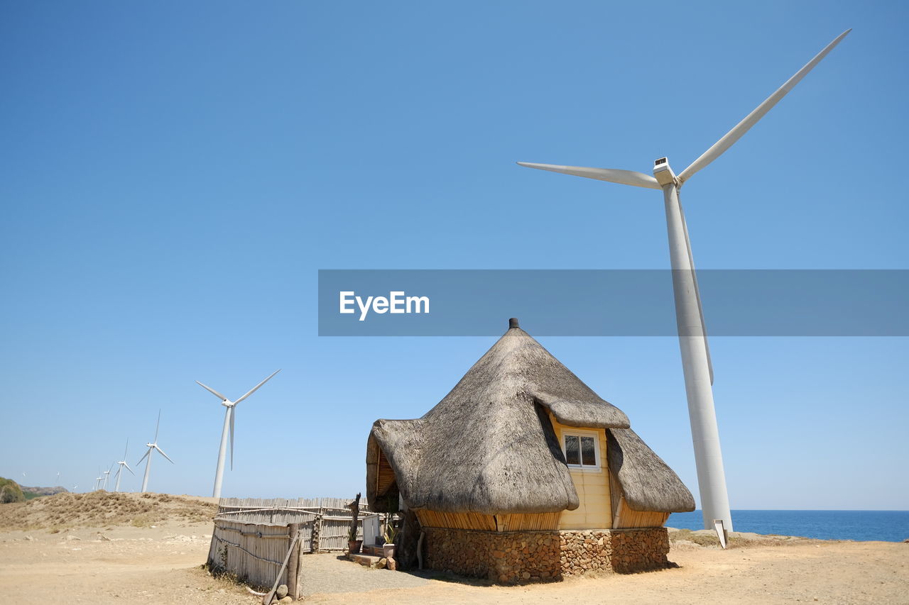 Wind turbines and house at beach against clear blue sky