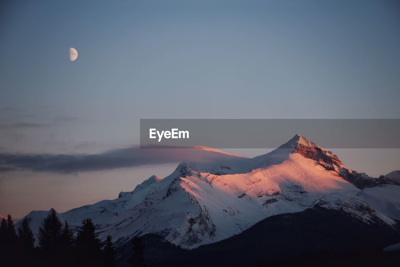 Scenic view of snowcapped mountains and moon during sunset