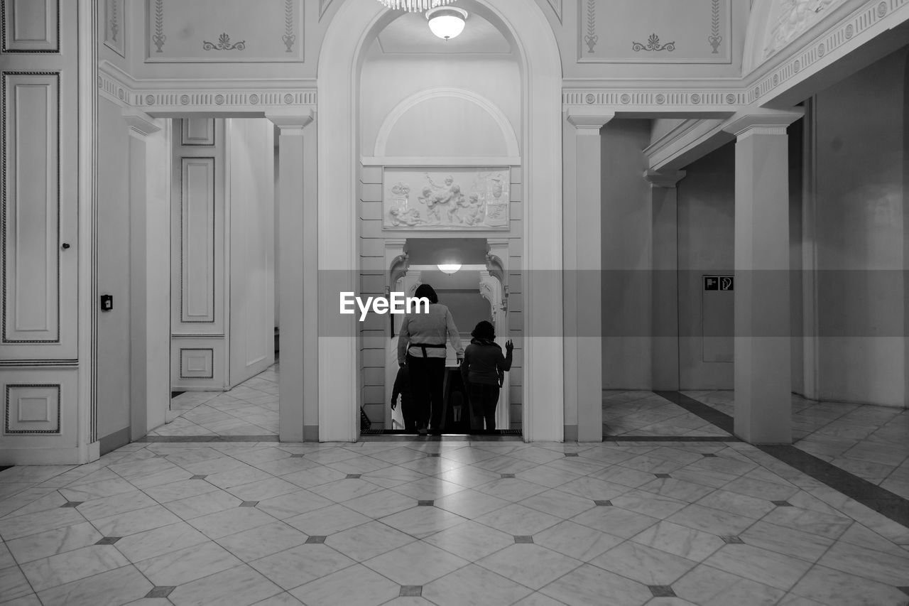 architecture, black and white, adult, built structure, entrance, building, full length, women, men, monochrome, door, arch, two people, rear view, white, arcade, corridor, indoors, monochrome photography, togetherness, lifestyles, religion, flooring, standing, architectural column, the past, mansion, history