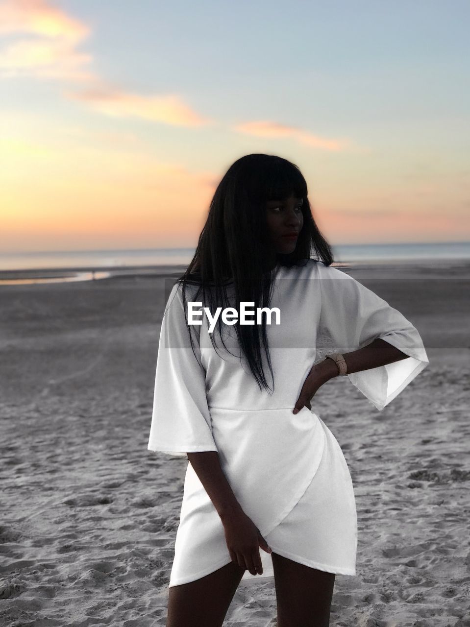 BEAUTIFUL WOMAN STANDING ON BEACH AGAINST SKY DURING SUNSET